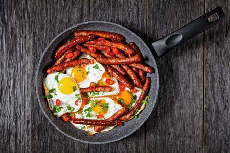 Longaniza con huevos, breakfast of sausages with fried eggs in a pan on a wooden table, horizontal view from above, mexican cuisine, flat lay, free spaceの写真素材