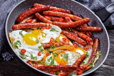 Longaniza con huevos, breakfast of sausages with fried eggs in a pan on a wooden table, horizontal view from above, mexican cuisineの写真素材