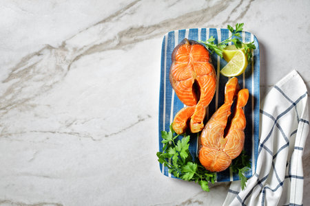 salmon steaks served with lemon wedges and parsley on a blue rectangular plate on a marble table, horizontal view from above, flat layの写真素材