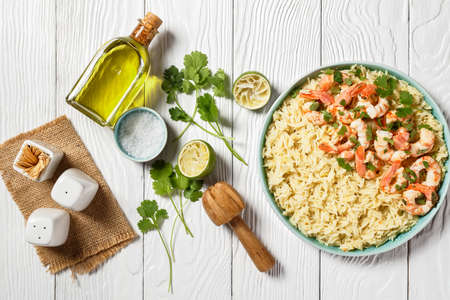 American cuisine lime shrimps with cilantro and long grain rice cooked with chicken broth served on a blue plate on a white wooden background with olive oil, top view, close-upの写真素材