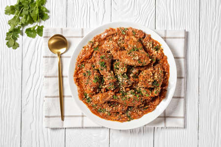 Chakhokhbili, stewed chicken, tomato with fresh herbs, walnuts and spices on a white plate on a wooden table, georgian cuisine, flat layの写真素材