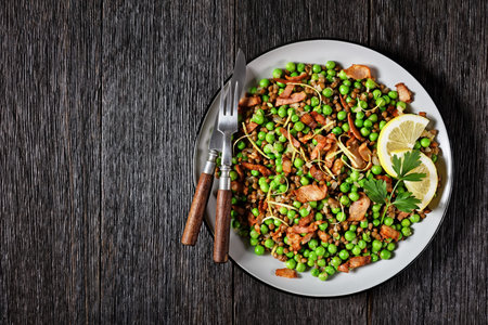 Lebanese warm lentil and green peas salad with bacon, lemon zest, and lemon and olive oil dressing served on a plate on a dark wooden background, top view, close-up, copy spaceの写真素材