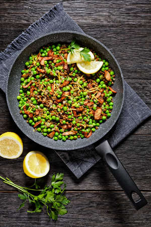 Lebanese warm lentil and green peas salad with bacon, lemon zest and lemon and olive oil dressing served on a frying pan on a dark wooden background, top view, close-upの写真素材