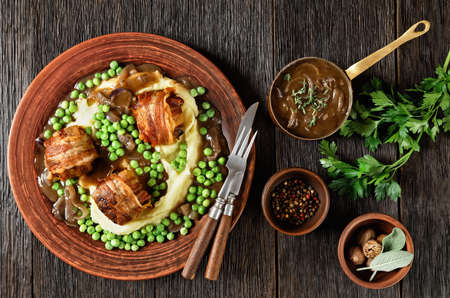 baked faggots served with creamy mashed potatoes, green peas and rich, thick onion gravy on a clay plate, british cuisine, flat layの写真素材