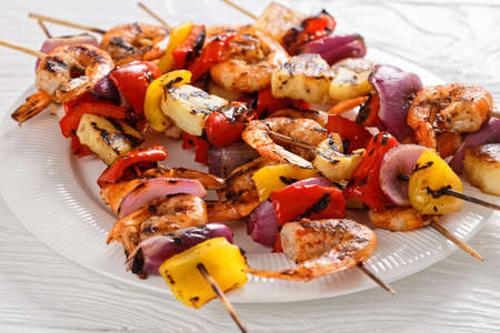 Pineapple Shrimp Kabobs with charred red onion, sweet pepper on a white plate, on a wooden table, close-upの写真素材