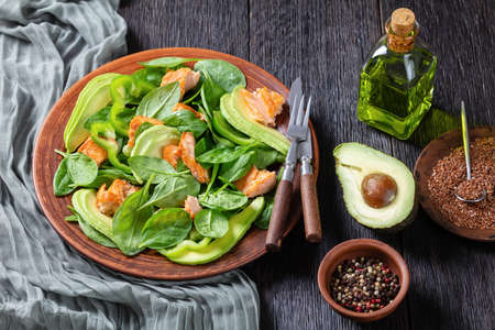 salmon spinach avocado and green pepper salad on a brown rustic plate with fork and knife on a bog oak table, mediterranean healthy dietの写真素材