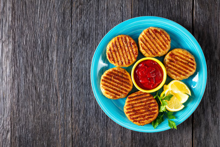 grilled fish burgers on a blue plate with tomato sauce and lemon wedges, flat lay, free spaceの写真素材