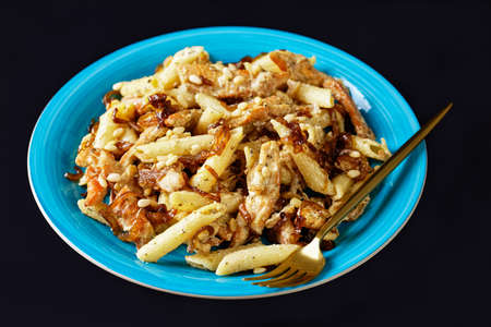 chicken alfredo pasta penne with caramelized onion sprinkled with pine nuts and grated parmesan cheese on a blue plate on black backgroundの写真素材