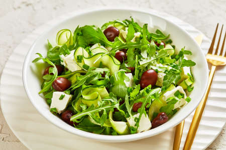 broad bean, feta cheese, rocket and cucumber salad in a white bowl on a white concrete table with golden cutleryの写真素材