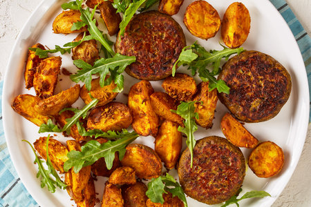 vegan lentil and bean burgers patties with baked potato wedges,  rocket leaves and hummus on a white...