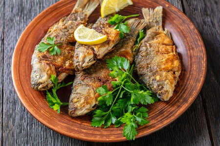 fried crucian carps with golden crispy crust on a clay rustic plate with parsley and lemonの写真素材