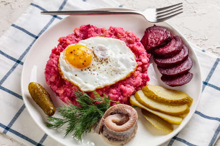 labskaus, corned beef, mashed potatoes with the beetroot topped with fried eggs, sliced beets, with pickles, and rollmops, pickled, rolled herring on a plate, german cuisineの写真素材