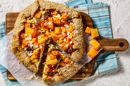 pumpkin galette with caramelized onion, cream cheese, thyme and crumbled feta cheese on a wood board
