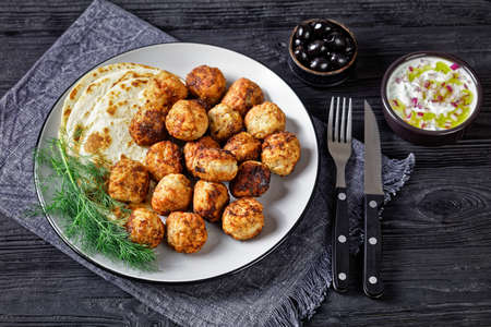 Keftedakia, fried greek meatballs with pita bread and dill on a grey plate on a black wooden table with tzatziki sauce, horizontal view from aboveの写真素材