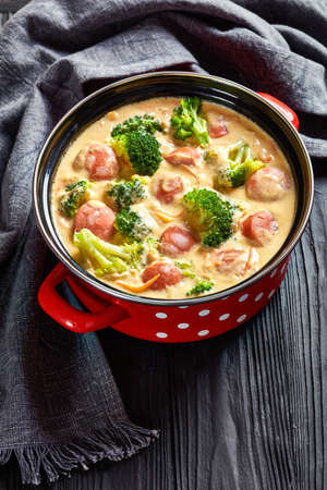 Creamy Sausage and Broccoli Cheese Vegetables Soup in a red pot on a black wooden table, vertical view, close-upの写真素材