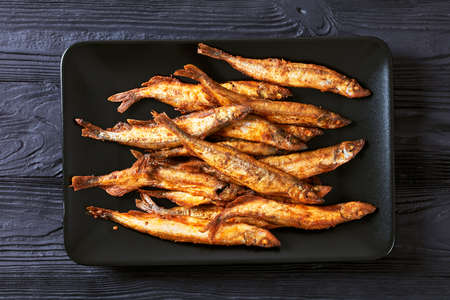 crispy fried capelin, shishamo on a black rectangular platter on a black textured wooden table, flat layの写真素材