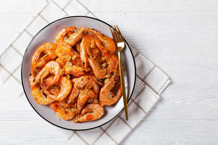 Grilled garlic butter prawns, Spanish Gambas al Ajillo on a plate on a white wooden table, flat lay, free spaceの写真素材