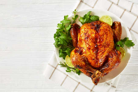 whole roast chicken, turkey with rosemary, mint, parsley and lime on a white plate on a wooden table, horizontal view from above, flat lay, free spaceの写真素材