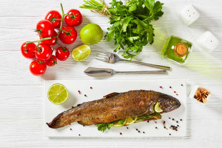 whole grilled trout fish with herbs and spices, served on a white rectangular platter with lime slices and parsleyの写真素材