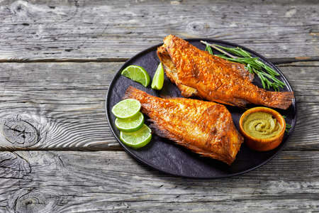 two fried ocean perch on a plate with rosemary and lime slicesの写真素材