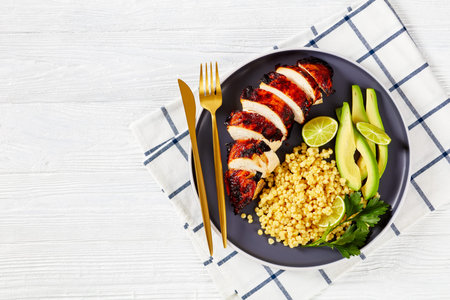 roasted chicken breast with pearl couscous, ptitim, fresh avocado and lime on a plate on a white...