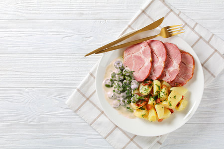Judd mat gaardebounen, Smoked pork neck with blanched young Fava Beans cooked with creamy sauce and boiled potatoes on a white plate, classic Luxembourg dish, horizontal view, flat lay, free spaceの写真素材