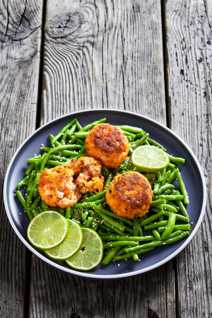 Thai Prawn and Crab Cakes on a plate with boiled green beans, lime on a wood table, vertical view...