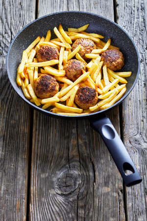 Vitoulet de Charleroi, Gehaktballetjes, Belgian meatballs of ground pork and veal in a skillet with french fries on a rustic wood table, vertical viewの写真素材