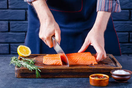 Man is cutting salmon fillet. Chef cutting a fish fillet on a rustic wooden board on a restaurant kitchen, close-upの写真素材