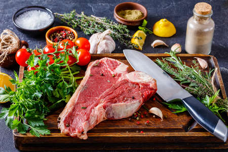 porterhouse beef steak with herbs, spices.  beef steak on a rustic wooden board with knife and ingredients for cooking, close-upの写真素材