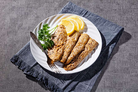 hot smoked spicy scomber fish fillets on a white plate with lemon slicesの写真素材