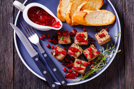 liver pate cubes on a plate with toasted baguette slices, thyme, cowberry sauce and fresh berries, horizontal view from above, flat lay, close-upの写真素材
