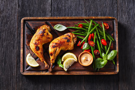 roast chicken legs with green beans, lemon, fried tomatoes, and mustard on rustic rude board with...