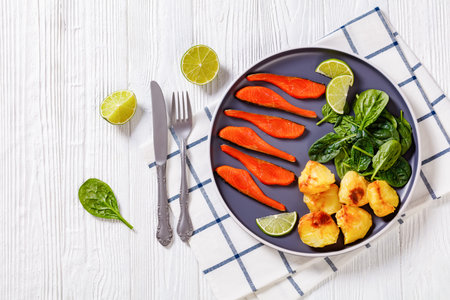 cold smoked salmon slices with fresh spinach leaves, roast potatoes and lime on plate, on white wooden table, flat lay, free spaceの写真素材