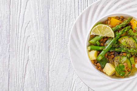 low calories alkaline green soup with spring vegetables, green lentils, chia seeds and herbs in white bowl on white wooden table, horizontal view from above, flat lay, free space, macroの写真素材