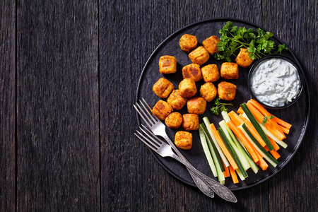 chickpea and veggies mini rolls or gnocchi served with fresh cucumber and carrot sticks and yogurt sauce with herbs on black plate with forks, flat lay, free spaceの写真素材