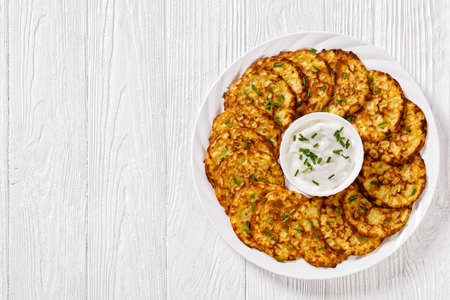 spelt flour pancakes with sour cream based sauce sprinkled with freshly chopped chives on white plate on white wooden table, horizontal view from above, flat lay, free spaceの写真素材