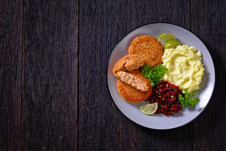 salmon patty with potato mash and beetroot salad on plate on dark wooden table, horizontal view from above, flat lay, free spaceの写真素材