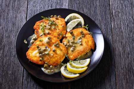 delicious chicken piccata of parmesan breaded seared chicken breasts with lemon butter caper sauce on black plate, horizontal view from aboveの写真素材