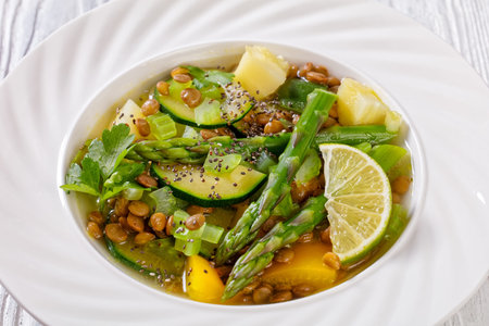 alkaline green soup with spring vegetables, green lentils, chia seeds and herbs in white bowl on...