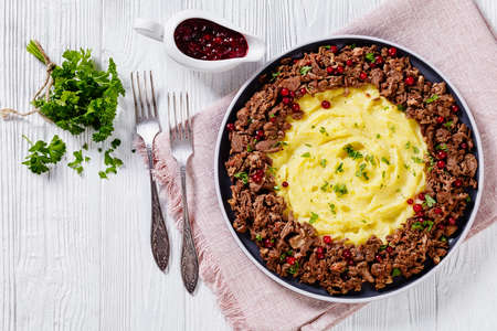 Reindeer Stew with Lingonberries and potato puree on plate on wood table with parsley and Lingonberry sauce on background, finnish cuisine, horizontal view from above, flat layの写真素材