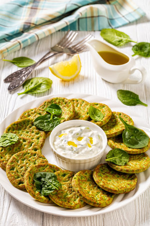 baked in oven spinach pancakes on white plate with tzatziki sauce on white wooden table, vertical...