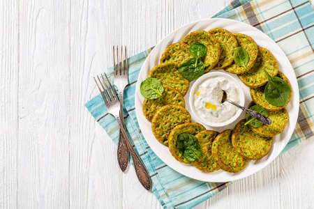 healthy spinach pancakes on white plate with tzatziki sauce on white wooden table, horizontal view from above, flat lay, free spaceの写真素材