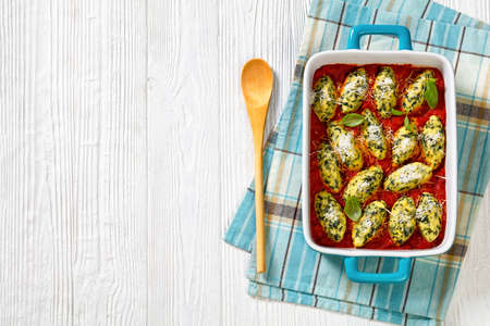 Malfatti, Italian spinach ricotta dumplings in tomato sauce with herbs and grated parmesan cheese in ceramic baking dish on white table, flat lay, free spaceの写真素材