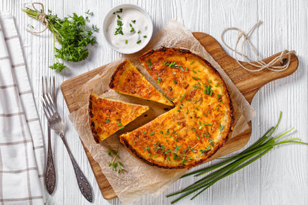 bacon and cheddar cheese quiche with hash brown crust on wood cutting board with forks on white...