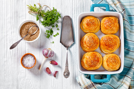 freshly baked snail shaped hand pies with ground mutton fillings in blue baking dish on white wooden...