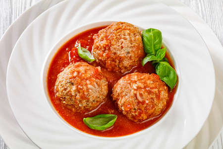 Italian Porcupine Balls, ground beef and rice meatballs in tomato sauce with basil leaves in white bowl, horizontal view from above, close-upの写真素材