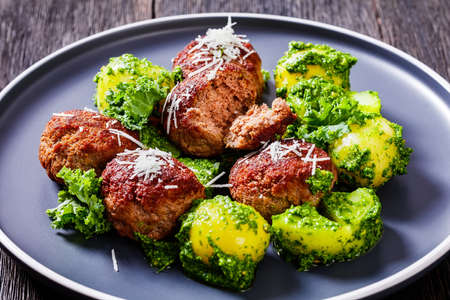 fried beef meatballs and boiled new potatoes coated with basil pesto on plate on dark wooden table, horizontal view from above, close-upの写真素材