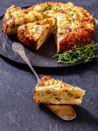 Cauliflower Cake with parmesan cheese, Basil and spices sliced on black platter on concrete table with a slice on cake shovel, vertical view from aboveの写真素材