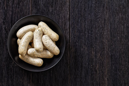 Weisswurst in black bowl, white sausages of minced veal, pork back bacon, spices and parsley, horizontal view from above, flat lay, free spaceの写真素材